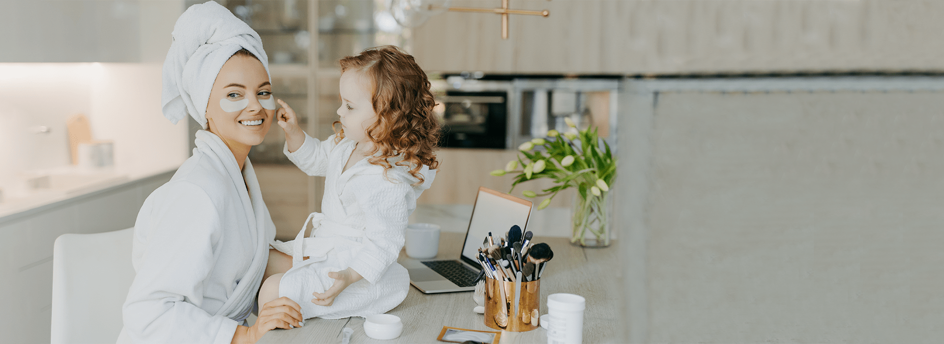 a girl in a white robe sitting on a table with a laptop and brushes